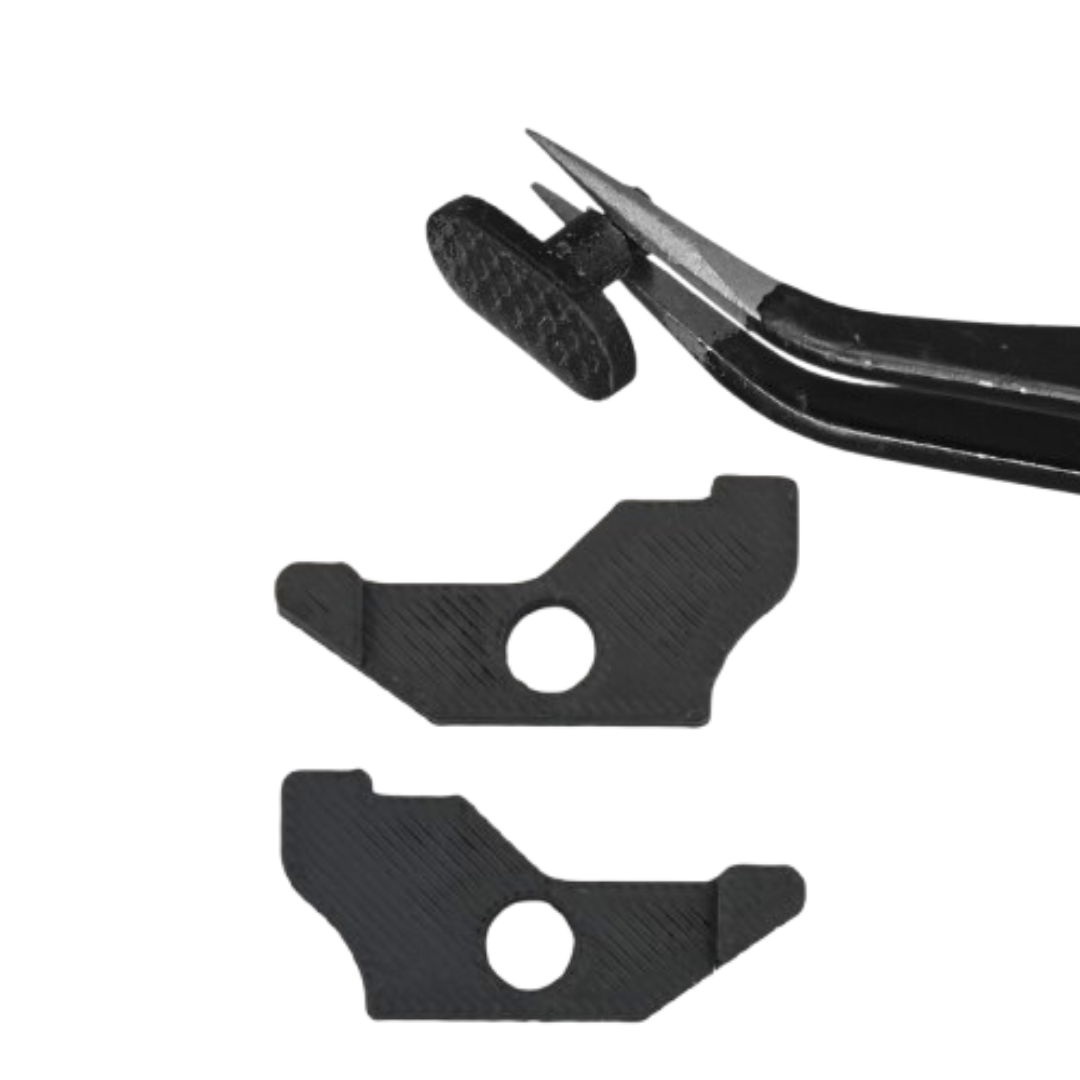 Black tweezers holding a small black plastic piece above two black plastic pieces with circular cutouts on a white background