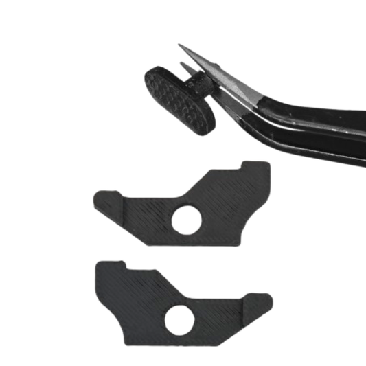 Black tweezers holding a small black plastic piece above two black plastic pieces with circular cutouts on a white background