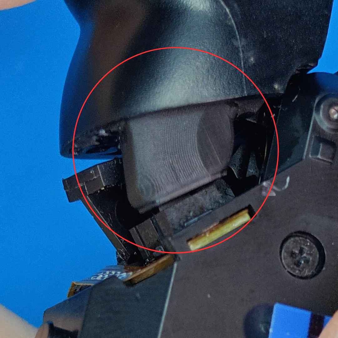 Close-up of the inside of a controller showing a black plastic trigger area, screw, ribbon cable, and a red circle highlighting a gray internal repair piece