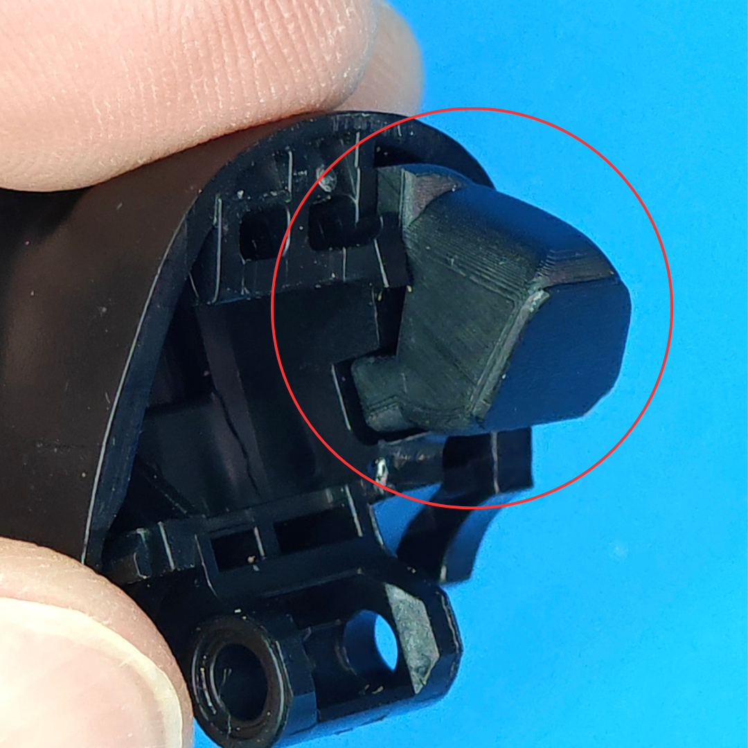 Close-up of a black plastic controller component held between fingers, with a red circle highlighting a trigger repair piece on a blue background