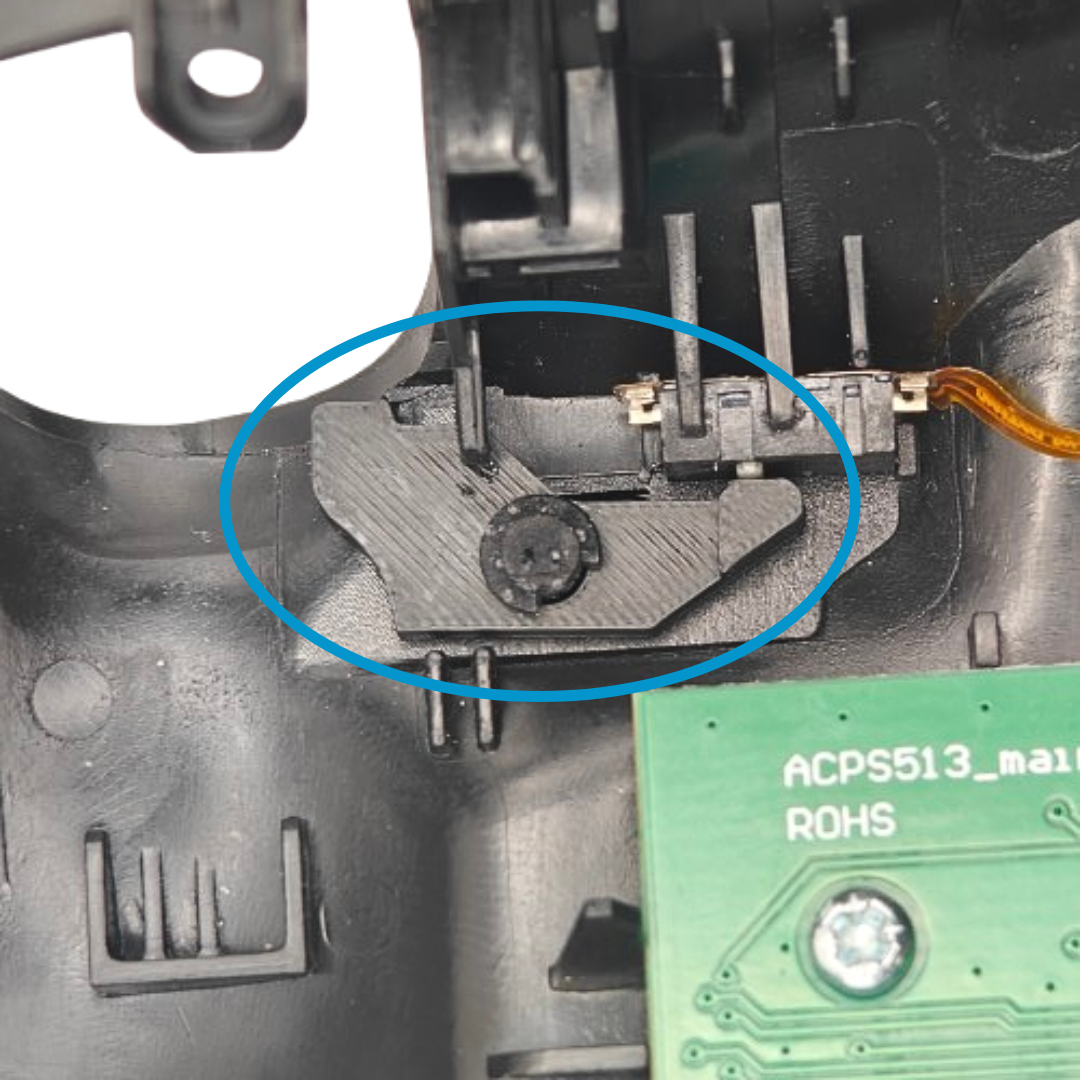 Close-up of the inside of a controller showing a black plastic piece, ribbon cable, circuit board, and a blue circle highlighting the installed piece
