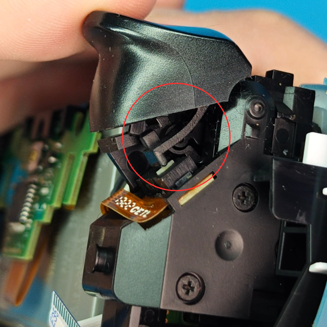 Close-up of the inside of a controller showing black plastic components, a ribbon cable, screws, and a red circle highlighting the trigger area