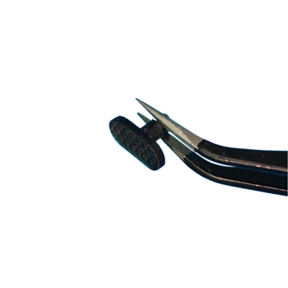 Black tweezers holding a small black plastic repair piece on a white background