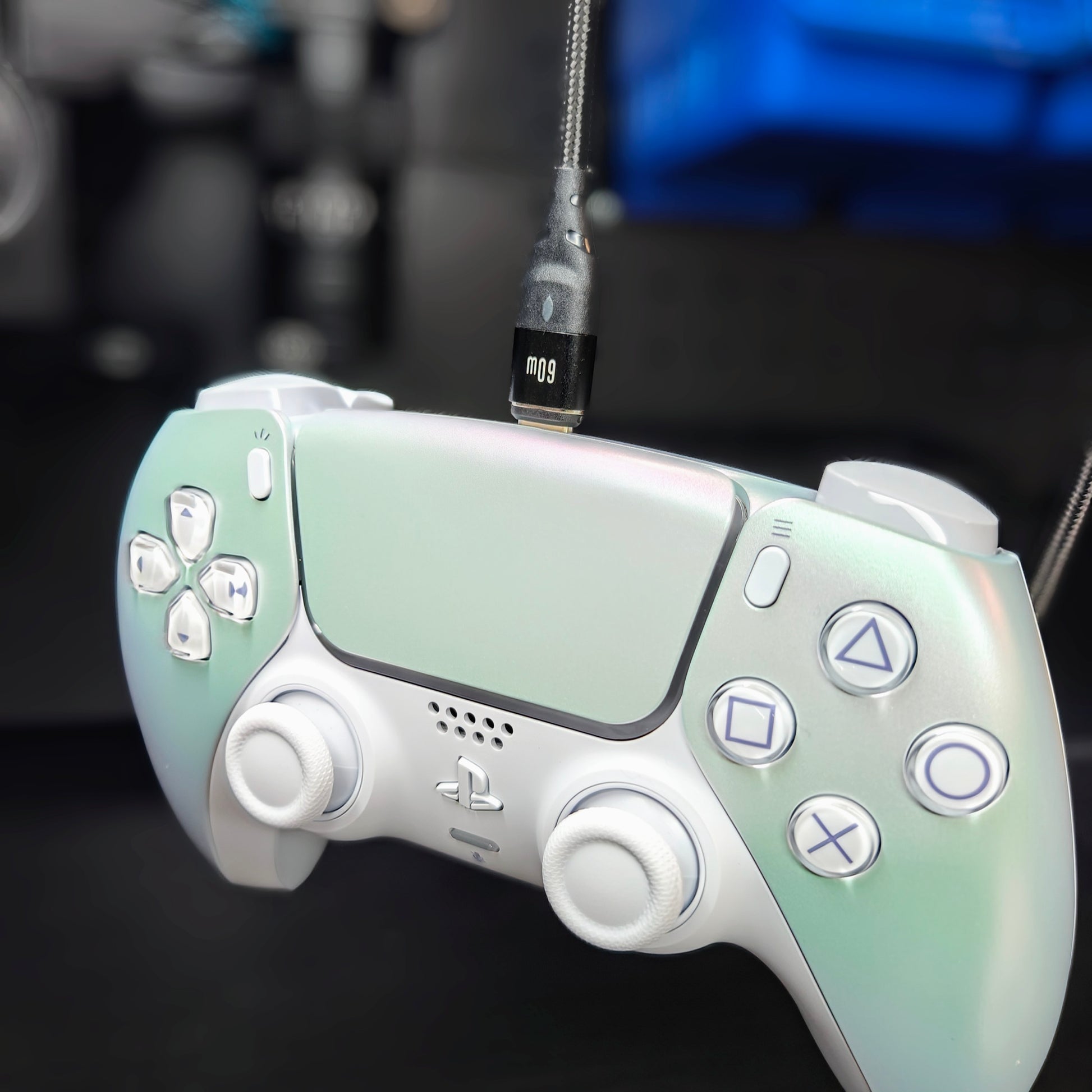 White iridescent controller with white thumbsticks and a magnetic charging cable attached at the top